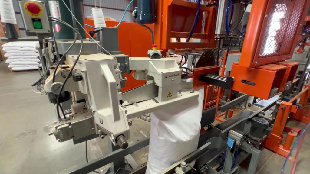 50 lb bag of nuts moving through a bag top reformer and bag sewing machine