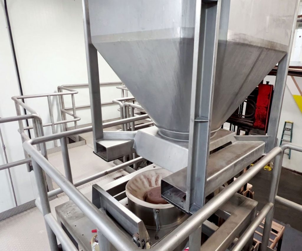 Lowering a stainless steel IBC container onto discharge station located above a vertical auger filling machine